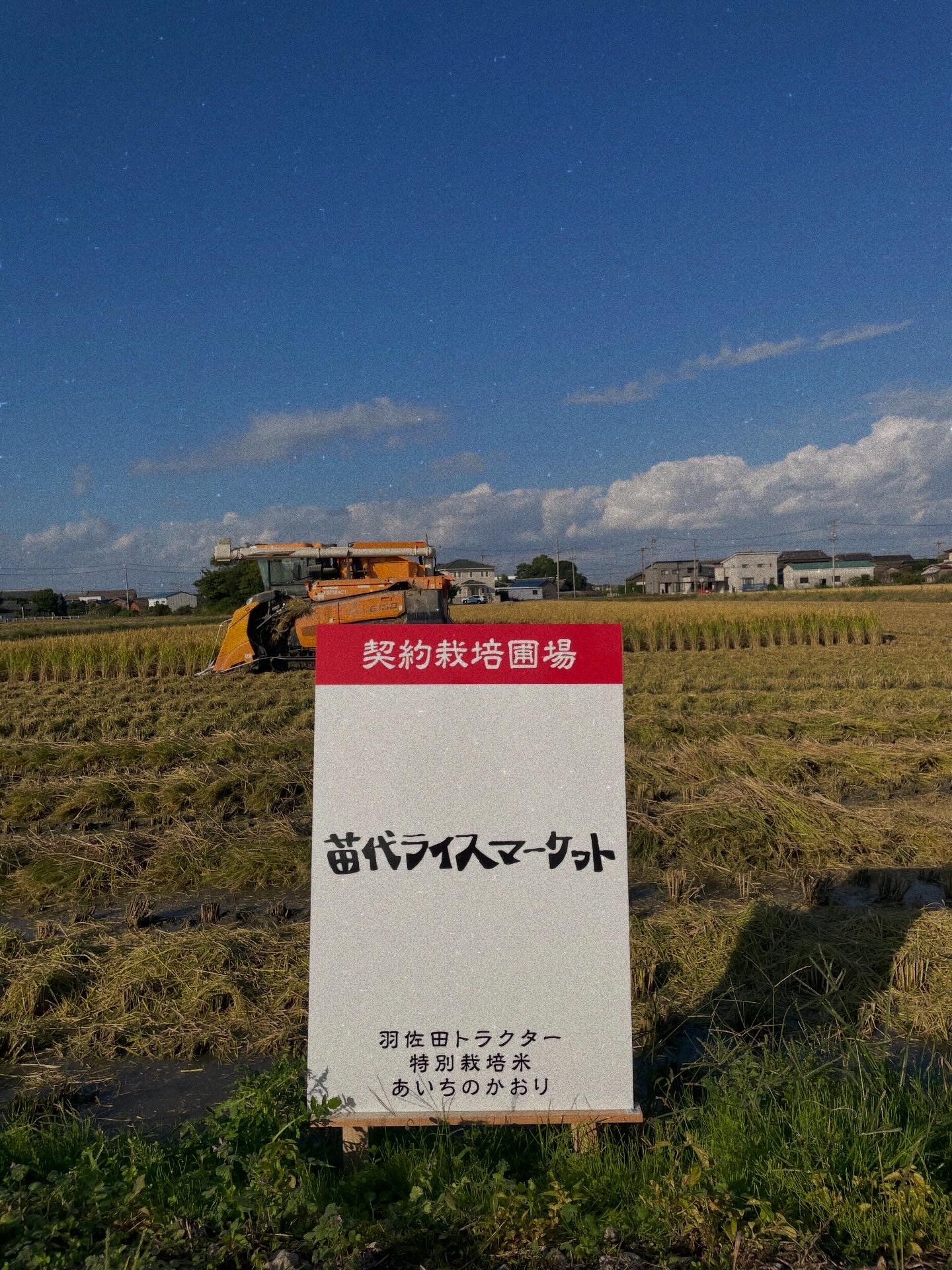 コンバインと苗代ライスマーケットの契約栽培圃場の看板